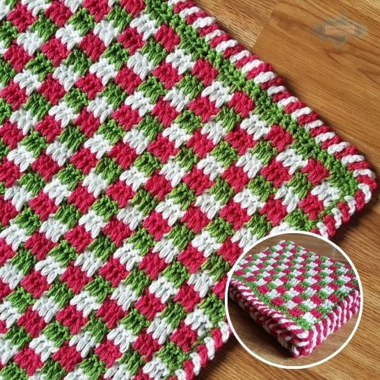 A close-up view of a vibrant crochet blanket with a checkered textured pattern using red, bright green, and white yarn, laid out on a wooden surface. A circular inset in the bottom right corner shows the entire blanket neatly folded, showcasing its festive holiday colors. This is a blanket pattern made by Ariana Wimsett of Crafting Happiness, a well known crocheter and author.