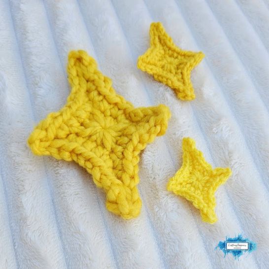 Three yellow crochet star appliques of varying sizes arranged on a soft, ridged white textured blanket. The stars have a distinct four-pointed shape with a raised, clean border along the edges.