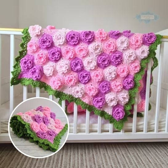 A vibrant baby blanket draped over a white wooden crib, completely covered in textured, three-dimensional crochet flowers in shades of pink, lavender, and deep purple. The entire blanket is framed by a bright green ruffled border resembling leaves. A circular inset in the bottom left corner shows the blanket neatly folded on a light floor, highlighting the thick texture of the floral motifs. This is a blanket pattern made by Ariana Wimsett of Crafting Happiness, a well known crocheter and author.