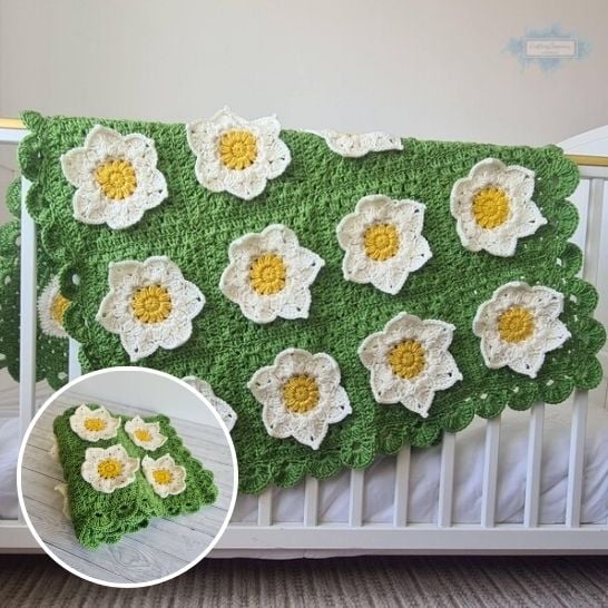 A bright green textured crochet blanket hanging over the side of a white crib. Large, three-dimensional white crochet waterlily flowers with bright yellow centers are appliquéd across the green surface, which is framed by a scalloped border. A circular inset in the lower left corner shows the blanket folded neatly on a light floor, showcasing the plush layering of the floral motifs. This is a blanket pattern made by Ariana Wimsett of Crafting Happiness, a well known crocheter and author.