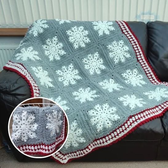 A winter-themed crochet blanket draped over a dark leather couch. The blanket is made of large squares in a medium gray yarn, each featuring a prominent, crisp white textured snowflake stitch in the center. The bottom and side borders are finished with a festive multi-colored trim of white, dark red, and bobby textures. A circular inset in the lower left corner shows a detailed close-up of the snowflake squares and the red-and-white border. This is a blanket pattern made by Ariana Wimsett of Crafting Happiness, a well known crocheter and author.