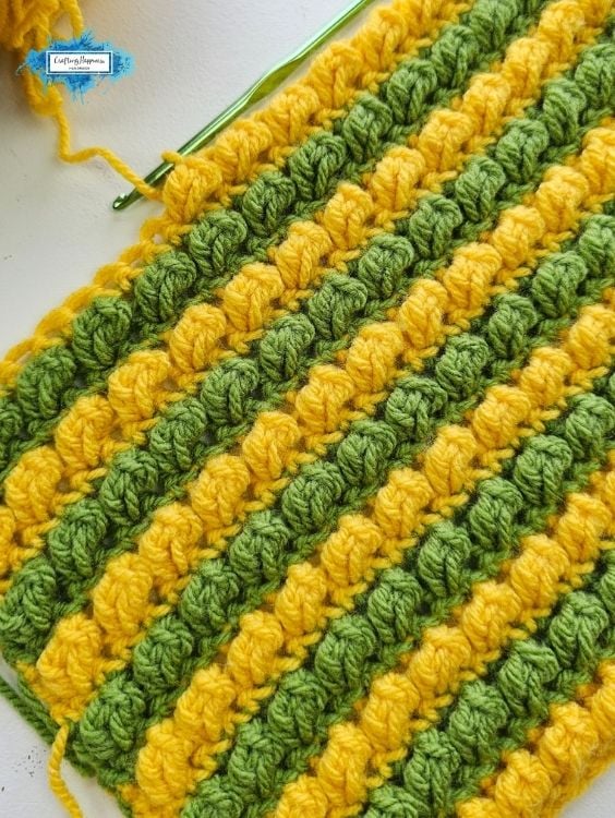 Alternating rows of yellow and green textured crochet stitches with a green crochet hook