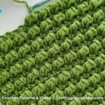 Close-up of green crocheted fabric with rows of raised, textured bobble stitches