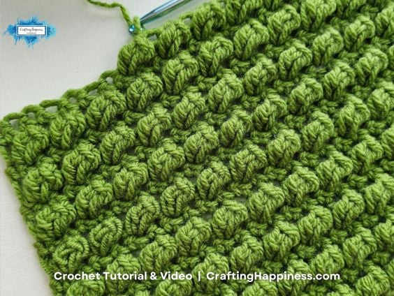 Close-up of green crocheted fabric with rows of raised, textured bobble stitches
