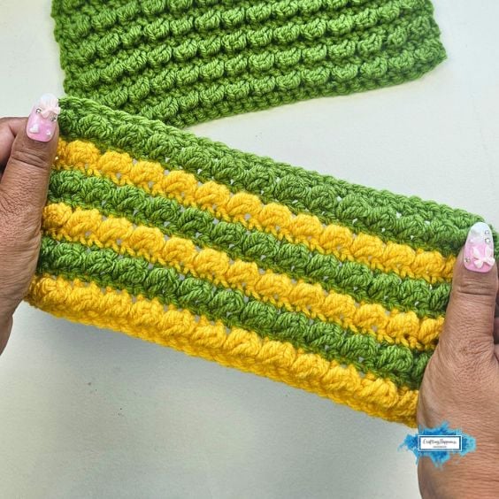 Hands holding a crochet swatch with alternating green and yellow stripes of textured bobble stitches
