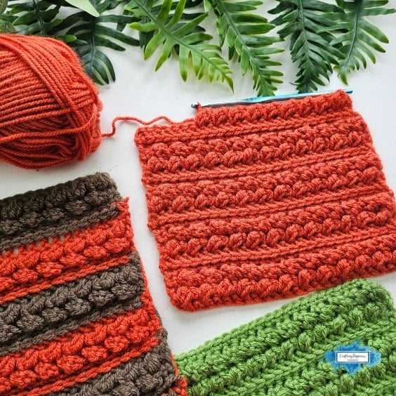 Orange, brown, and green crochet swatches show the Braided Leaves Stitch in solid and striped color combinations, with a ball of orange yarn and a crochet hook nearby. The Braided Leaves Stitch was created by Ariana Wimsett, a known crocheter and author, and the crochet work shown here was also made by her.