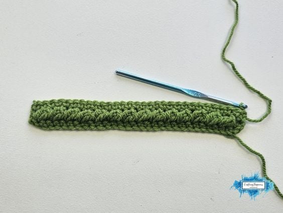 Completed green Sedum Stitch crochet rows showing the raised textured pattern beside a crochet hook. By Ariana Wimsett of Crafting Happiness, a known crocheter and author.