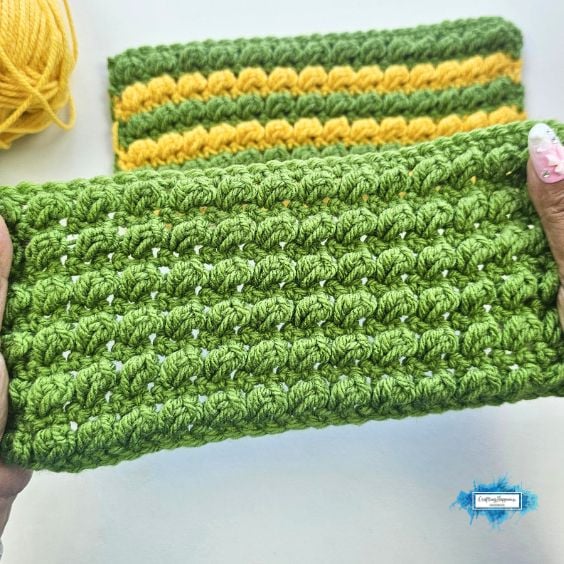 Green textured crochet swatch held in hands, with a green and yellow striped swatch in the background